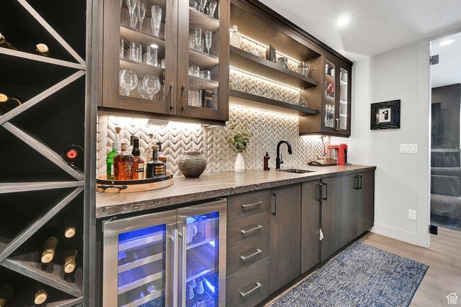 Indoor wet bar featuring beverage cooler, Ice maker, luxury backsplash, light wood flooring, and custom cabinets | Image 43