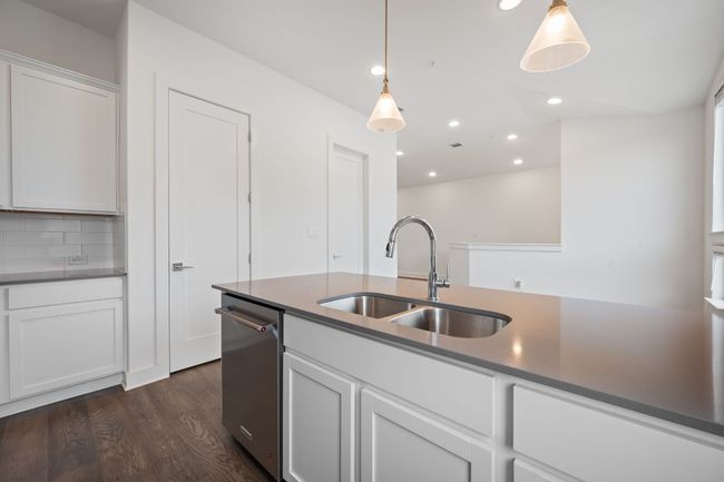 Kitchen featuring dark wood-style flooring, white cabinetry, stainless steel dishwasher, backsplash, and recessed lighting | Image 11