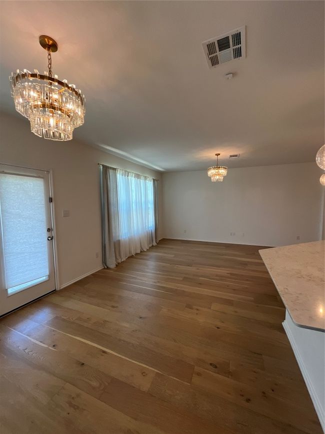Unfurnished dining area with a notable chandelier, wood finished floors, and visible vents | Image 12