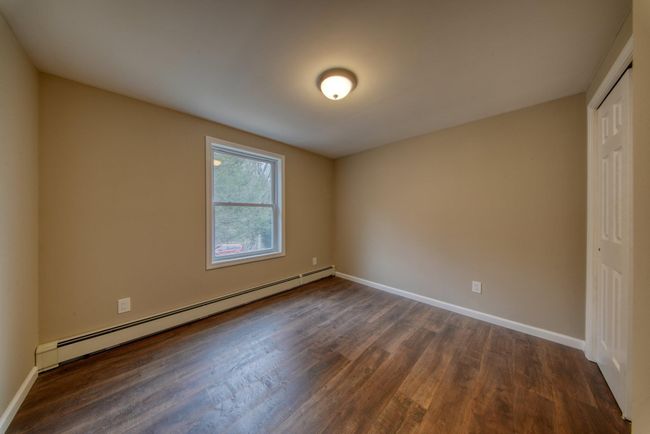Empty room with a baseboard radiator, baseboards, and dark wood-style flooring | Image 21