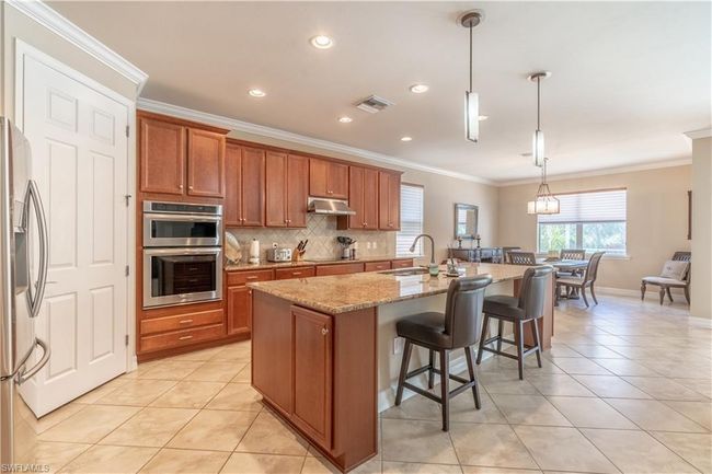 Kitchen featuring backsplash, light stone countertops, appliances with stainless steel finishes, sink, and ornamental molding | Image 11