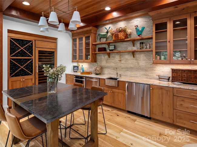 Entertainment kitchen features a full bar area with open shelves, double drawer dish washer, beverage cooler, built-in microwave, hammered brass bar sink and beautiiul wood cabinets with glass fronts. Flanking the bar is a Subzero 150 bottle wine cooler. | Image 29