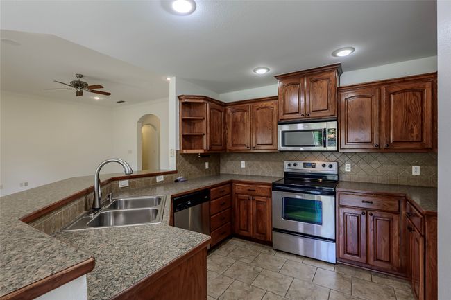 Kitchen featuring arched walkways, a sink, ceiling fan, open shelves, and appliances with stainless steel finishes | Image 22