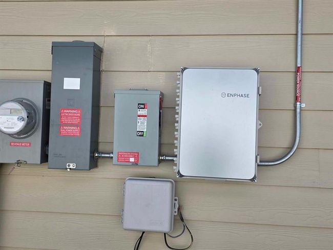 This photo shows an exterior wall with a solar power system setup, including an Enphase inverter, electrical panels, and a revenue meter, indicating the home is equipped with solar energy capabilities. | Image 26