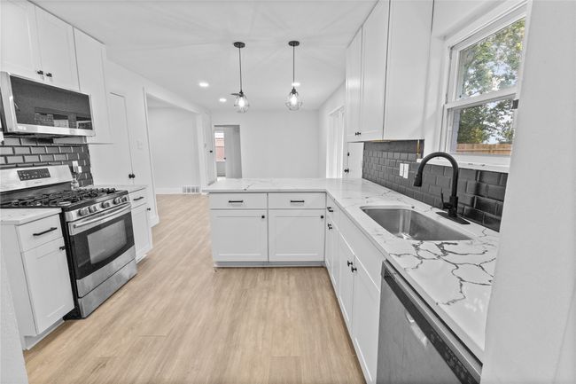 Kitchen with appliances with stainless steel finishes, a sink, a peninsula, white cabinets, and backsplash | Image 9