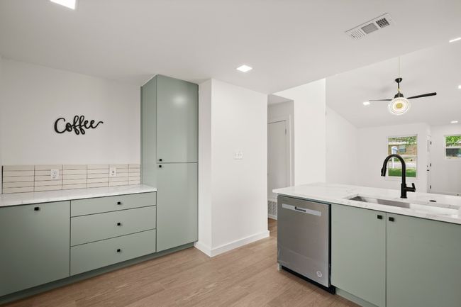 Kitchen featuring dishwasher, green cabinetry, light wood finished floors, ceiling fan, and light stone countertops | Image 26