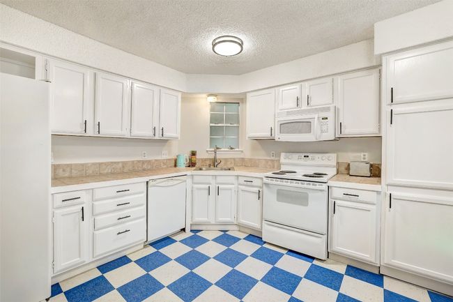 Kitchen featuring white appliances, light floors, white cabinetry, light countertops, and a textured ceiling | Image 6