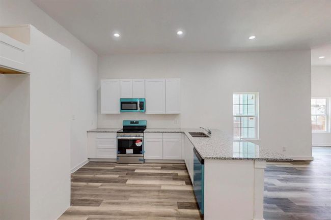 Kitchen featuring appliances with stainless steel finishes, light hardwood / wood-style floors, kitchen peninsula, and light stone counters | Image 14