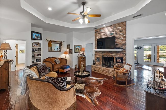 Living area with ceiling fan, a tray ceiling, visible vents, hardwood / wood-style floors, and a brick fireplace | Image 4