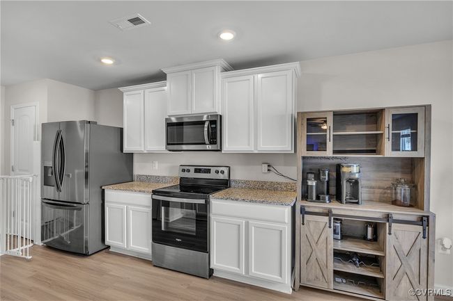 Kitchen with white cabinetry, appliances with stainless steel finishes, open shelves, and visible vents | Image 8
