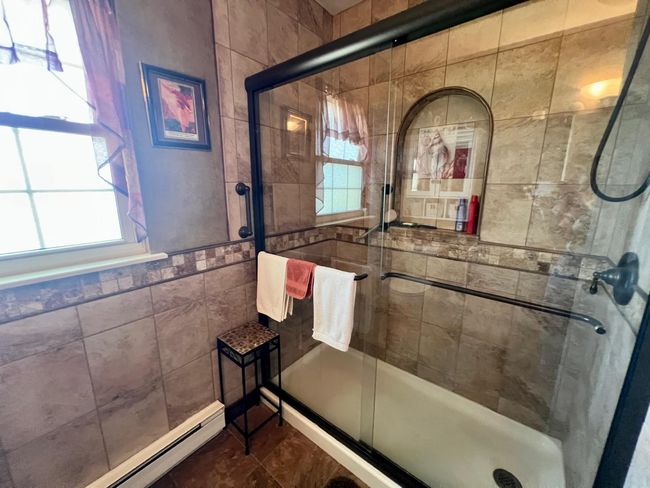 Bathroom featuring a baseboard radiator, plenty of natural light, tile walls, and a stall shower | Image 15