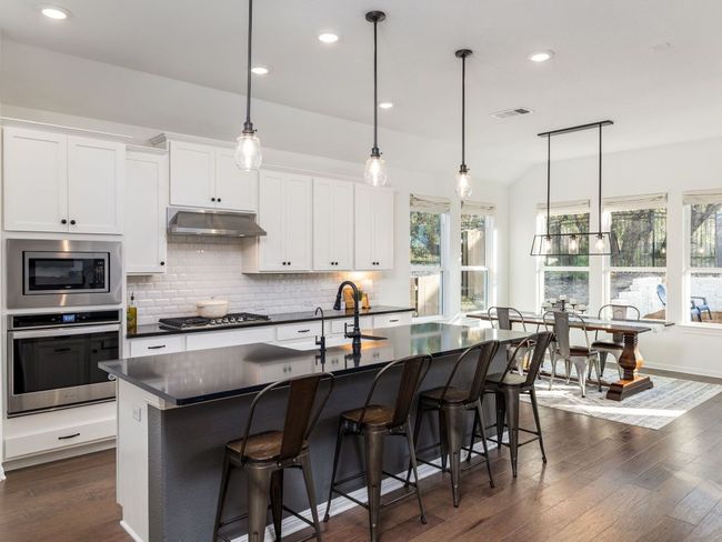 Kitchen featuring dark wood finished floors, appliances with stainless steel finishes, under cabinet range hood, dark countertops, and backsplash | Image 6