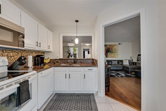 Kitchen featuring white appliances, white cabinetry, decorative light fixtures, light tile patterned flooring, and decorative backsplash | Image 10