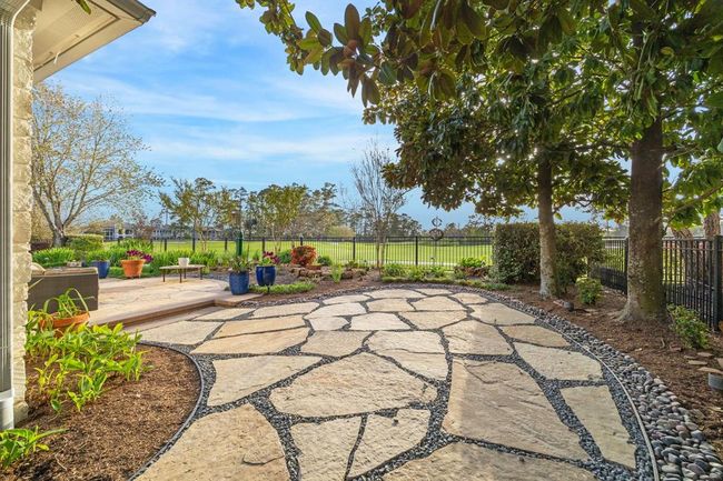 This backyard features a spacious stone patio surrounded by lush greenery and mature trees, offering a serene view. Ideal for relaxation and outdoor entertaining. | Image 38