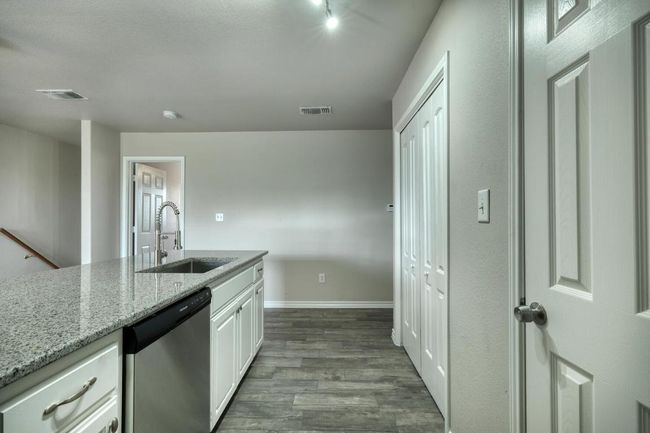 Kitchen with stainless steel dishwasher, dark wood-type flooring, light stone counters, and white cabinets | Image 8