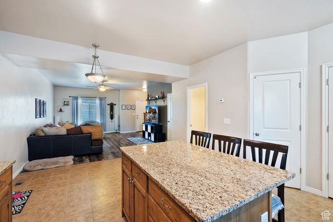 Kitchen featuring brown cabinets, ceiling fan, hanging light fixtures, light stone countertops, and a kitchen breakfast bar | Image 7