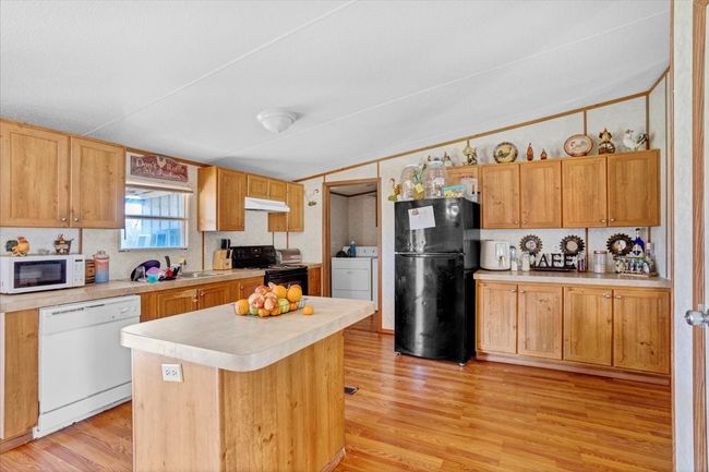 Kitchen with under cabinet range hood, vaulted ceiling, light countertops, black appliances, and light wood finished floors | Image 8