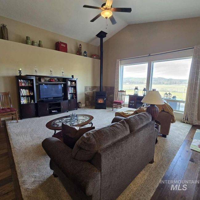 Living area with a wood stove, wood finished floors, a ceiling fan, and vaulted ceiling | Image 4