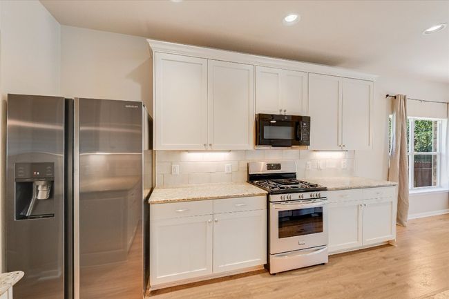 Kitchen with appliances with stainless steel finishes, recessed lighting, white cabinetry, light wood finished floors, and backsplash | Image 7