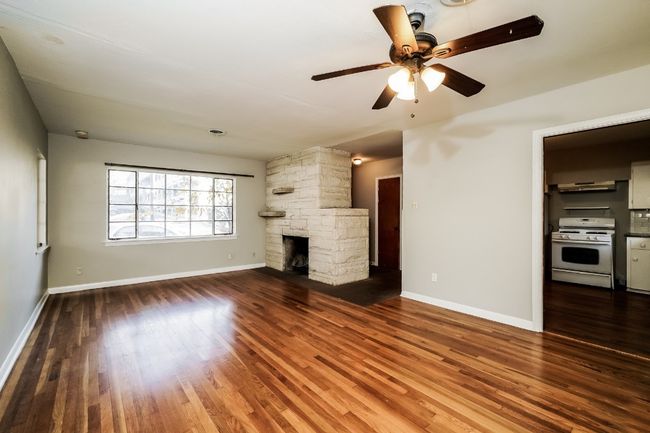 Unfurnished living room with wood finished floors, ceiling fan, and a fireplace | Image 7