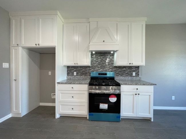 Kitchen with stainless steel gas stove, tasteful backsplash, custom exhaust hood, and white cabinetry | Image 11