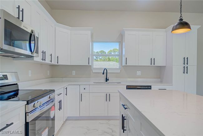 Kitchen with white cabinets, marble finish floor, stainless steel appliances, a sink, and hanging light fixtures | Image 8