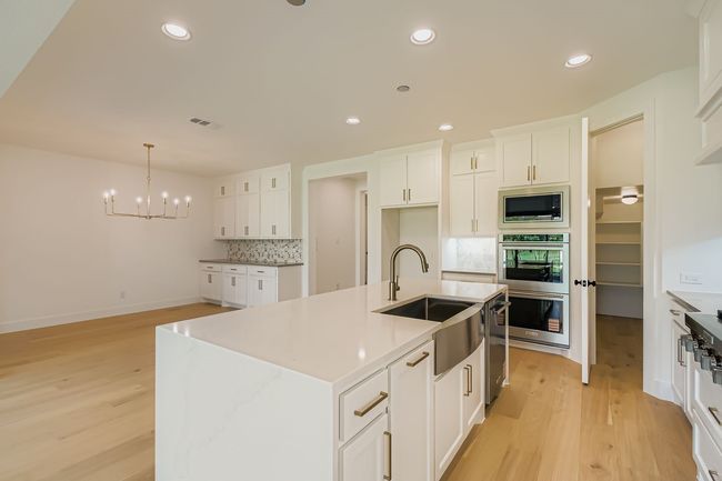 Kitchen featuring white cabinetry, recessed lighting, a center island with sink, light wood finished floors, and pendant lighting | Image 9