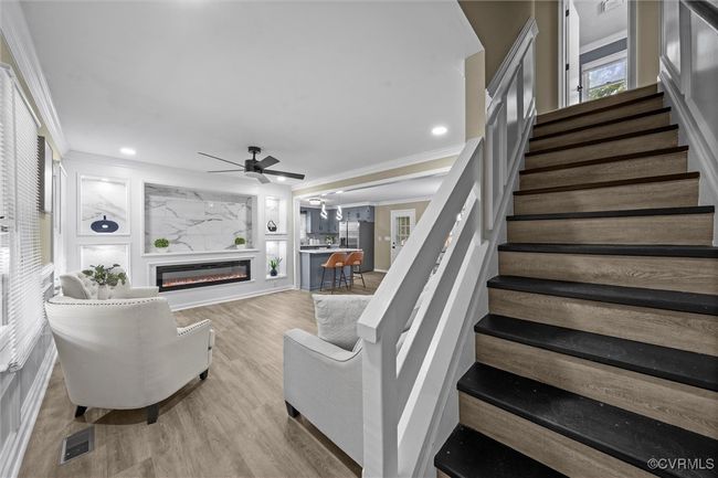 Living room featuring ornamental molding, stairway, a glass covered fireplace, a ceiling fan, and light wood-style flooring | Image 10