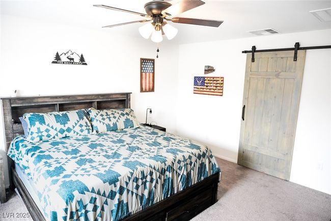 Carpeted bedroom with a barn door, ceiling fan, and visible vents | Image 23
