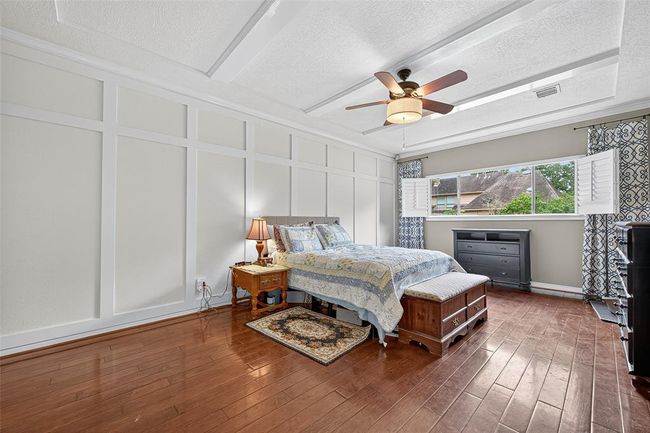 The primary bedroom glows with natural light through a wide window framed by plantation shutters. Embossed wall and ceiling paneling, along with hardwood flooring, add a sense of timeless texture and depth. | Image 38