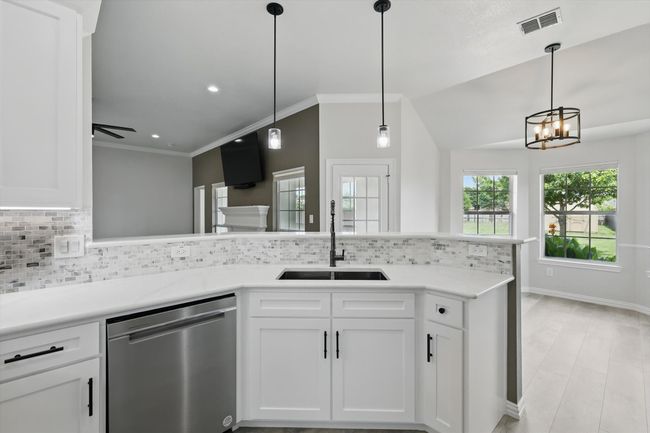 Kitchen with dishwasher, a sink, decorative backsplash, white cabinetry, and a chandelier | Image 13