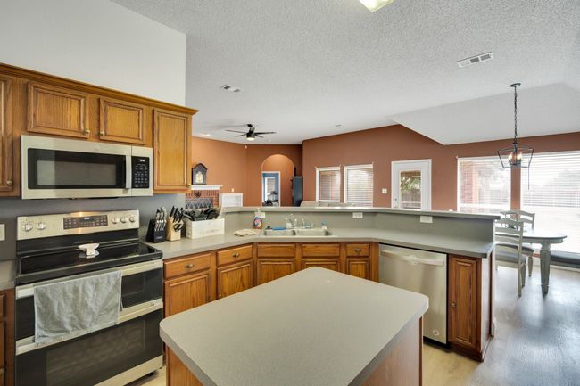 Kitchen with stainless steel appliances, a peninsula, brown cabinetry, light wood-style flooring, and a textured​​‌​​​​‌​​‌‌​‌‌​​​‌‌​​‌‌​‌​​​​​‌ ceiling | Image 14