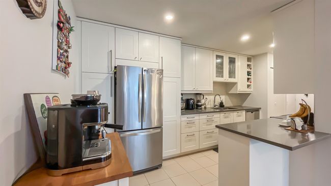 Kitchen with glass insert cabinets, a sink, appliances with stainless steel finishes, dark countertops, and white cabinetry | Image 6