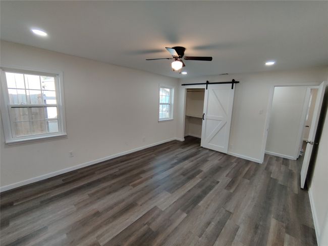 Unfurnished bedroom with ceiling fan, wood-type flooring, and a barn door | Image 12