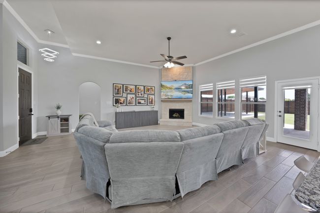 Living area with arched walkways, a ceiling fan, crown molding, a large fireplace, and baseboards | Image 9