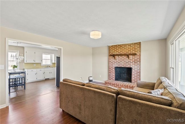 Living room featuring baseboards, dark wood-style flooring, a notable chandelier, and a brick fireplace | Image 14
