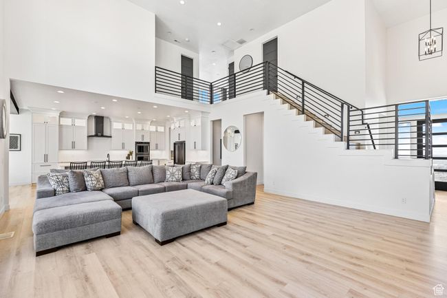 Living room featuring a towering ceiling, baseboards, a chandelier, stairway, and light wood-style flooring | Image 12