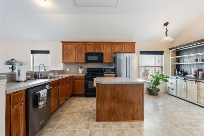 Kitchen with decorative backsplash, black appliances, light countertops, and a sink | Image 13