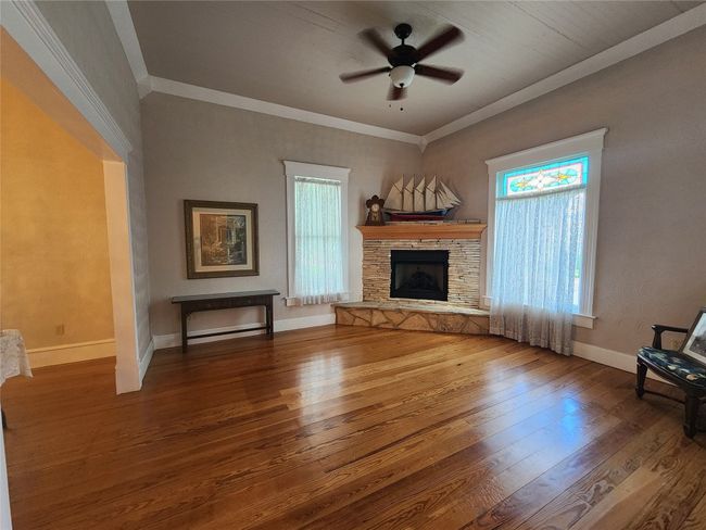 Unfurnished living room with hardwood / wood-style floors, a ceiling fan, a stone fireplace, and crown molding | Image 9
