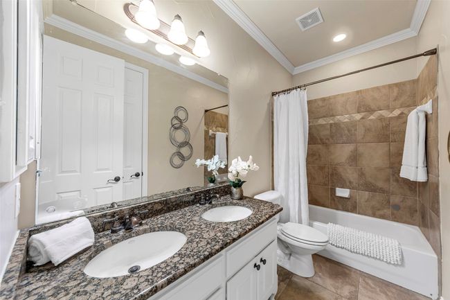 Bathroom featuring double vanity, shower / bathtub combination with curtain, toilet, tile patterned flooring, and ornamental molding | Image 27