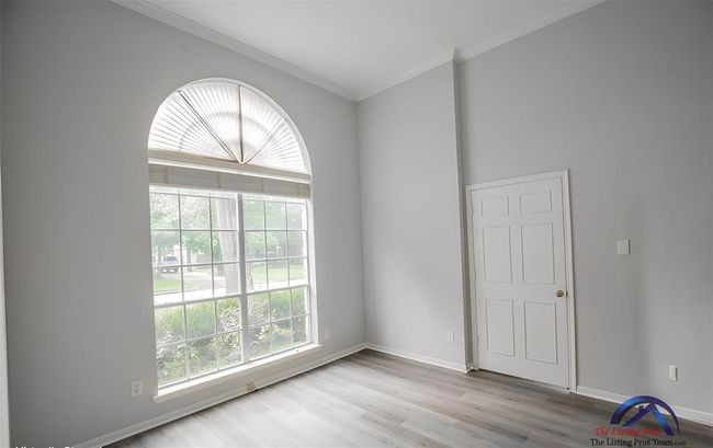 Bright room with high ceilings, featuring a large arched window for plenty of natural light. Fresh, neutral paint and sleek flooring create a modern feel, with an interior door adding functionality. Ideal for a home office or cozy retreat. | Image 10