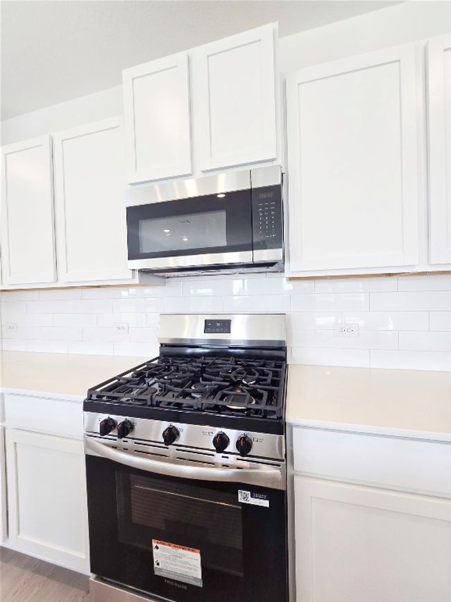 Kitchen with stainless steel appliances, light countertops, backsplash, and white cabinets | Image 23