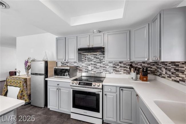 Kitchen featuring stainless steel appliances, under cabinet range hood, a raised ceiling, light countertops, and tasteful backsplash | Image 6