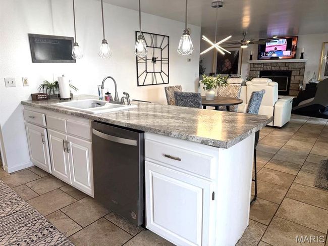 Kitchen featuring stainless steel dishwasher, a sink, a stone fireplace, white cabinets, and ceiling fan | Image 16