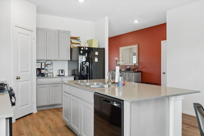 Kitchen with a sink, light wood-style floors, light countertops, black appliances, and an island with sink | Image 12