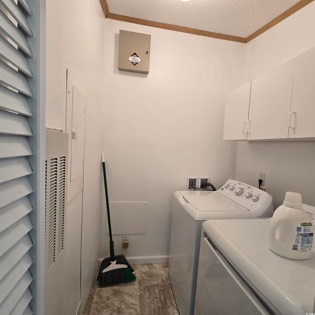 Washroom with cabinet space, crown molding, a textured ceiling, and washing machine and clothes dryer | Image 31