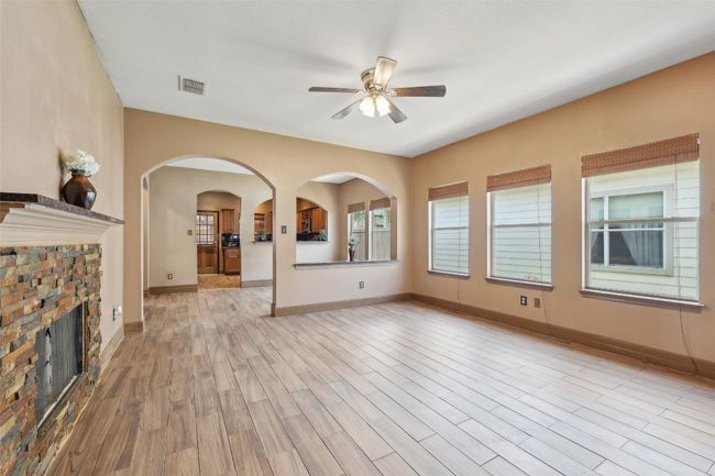 Unfurnished living room with a ceiling fan, light wood-style flooring, arched walkways, baseboards, and a fireplace | Image 5