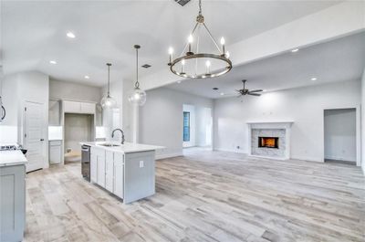 Kitchen featuring hanging light fixtures, a fireplace, ceiling fan with notable chandelier, sink, and an island with sink | Image 3