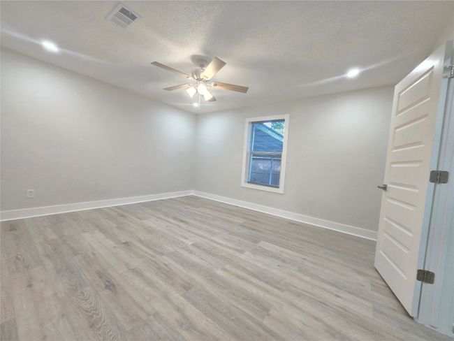 Empty room with a ceiling fan, light wood-style floors, a textured ceiling, and recessed lighting | Image 15