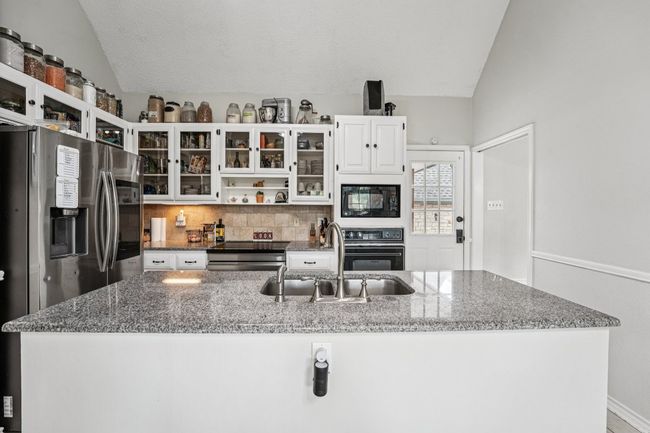 Kitchen featuring black appliances, lofted ceiling, tasteful backsplash, dark stone countertops, and white cabinets | Image 10